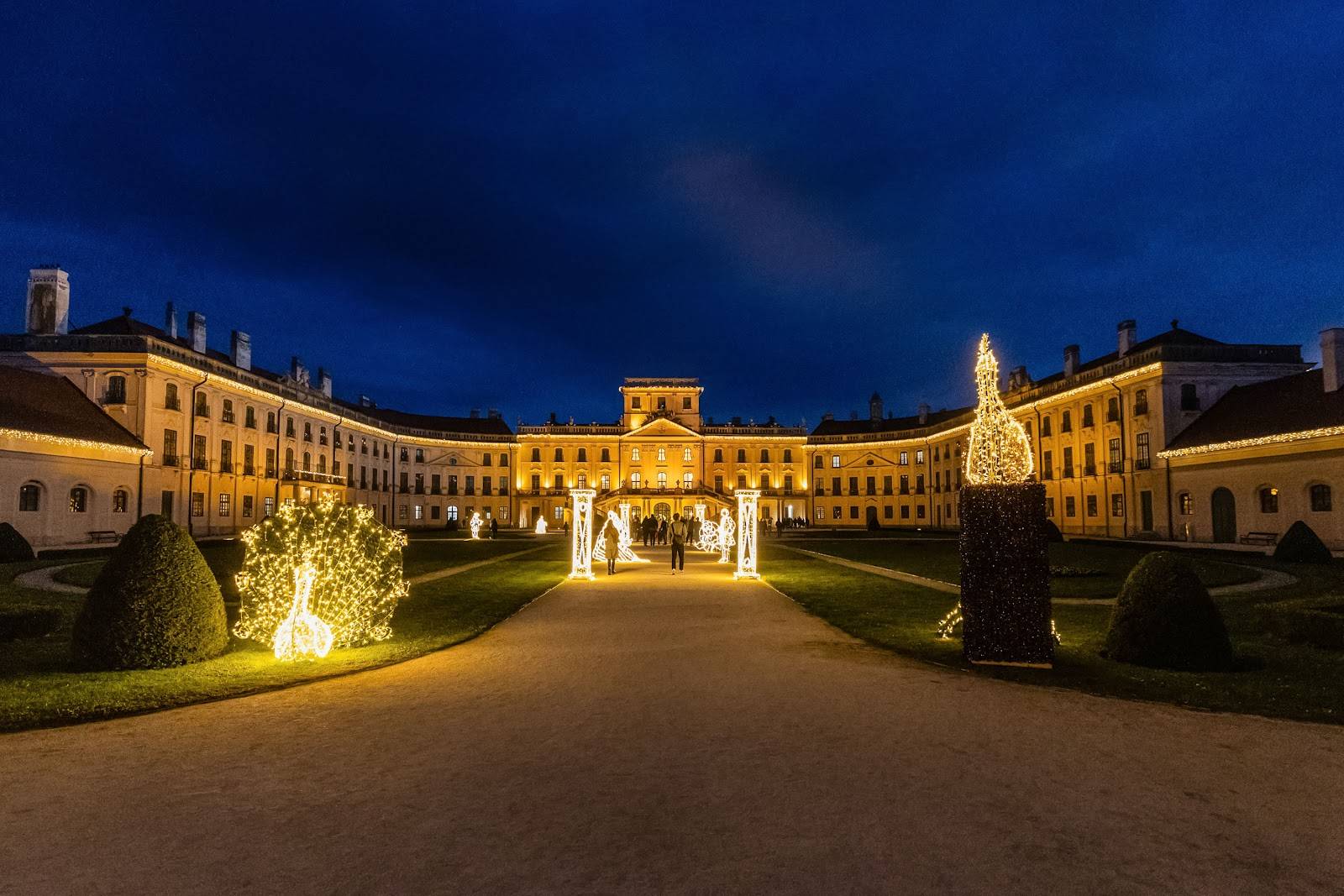 Lichtpark am Schloss Esterházy mit einem beleuchteten Pfau und Lichttoren in der Dämmerung.